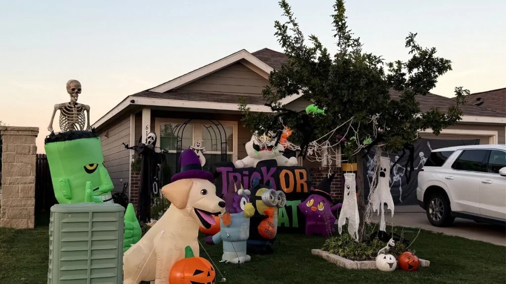 Halloween yard display with inflatables, skeletons, and pumpkins outside a home
